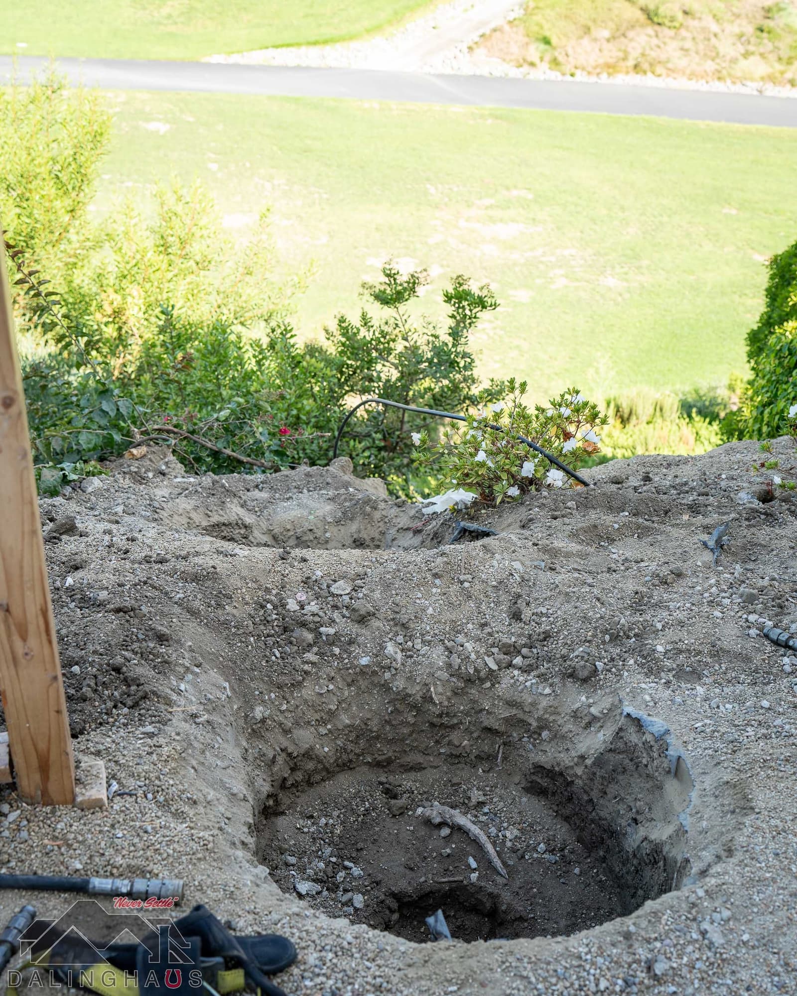 Hand dug pit at the edge of a hillside backyard, green slope and path far below