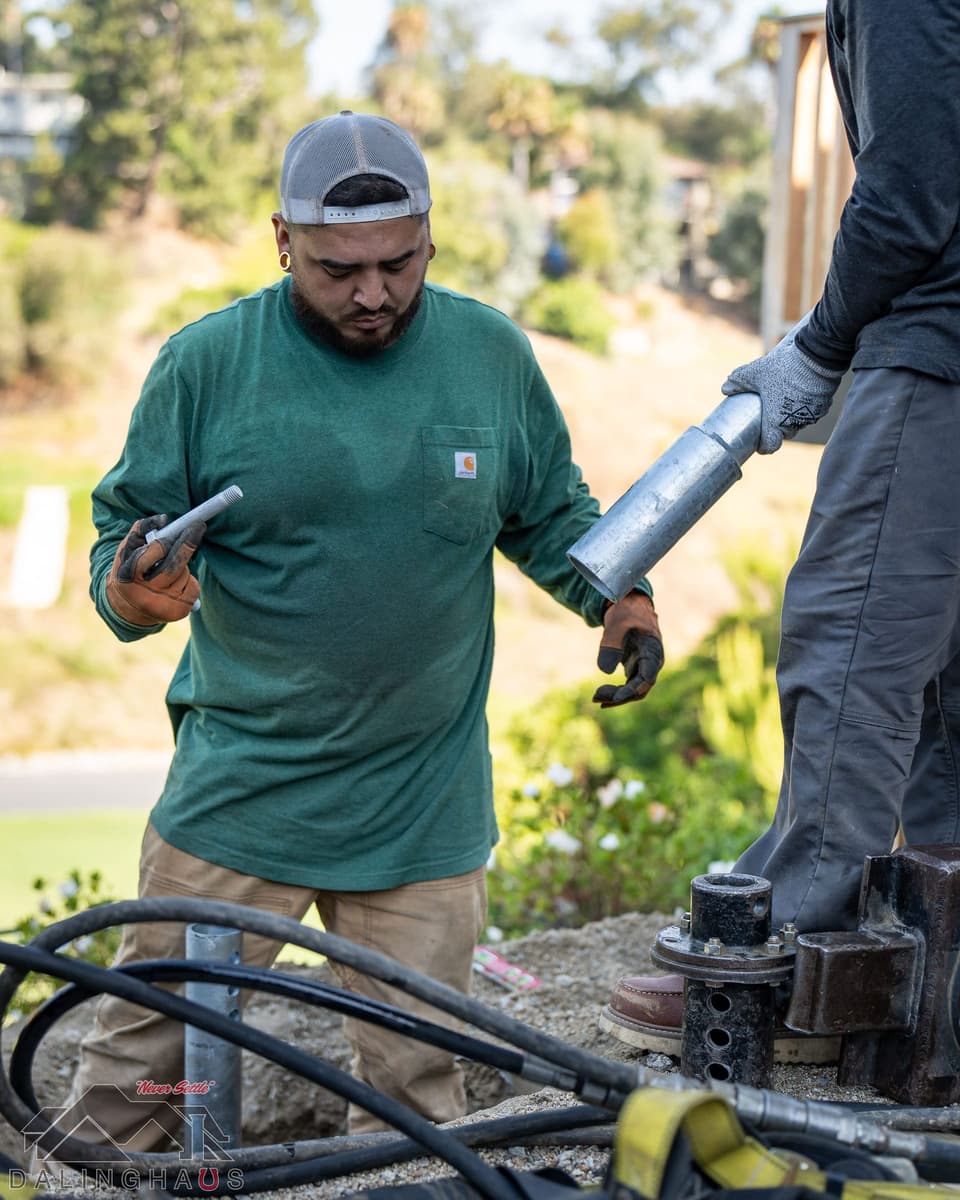 Crew member in a green shirt receiving a galvanized extension section while holding a coupler bolt