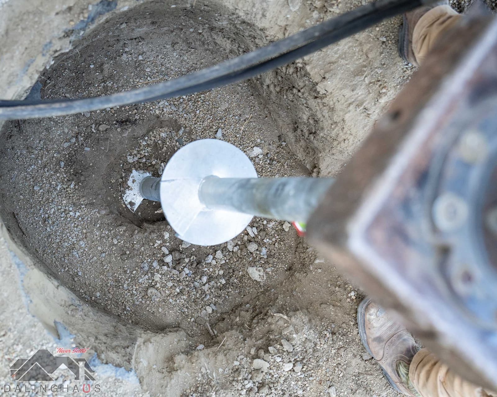 Helix plate on a galvanized pier shaft at the floor of a hand dug pit, work boot at the edge