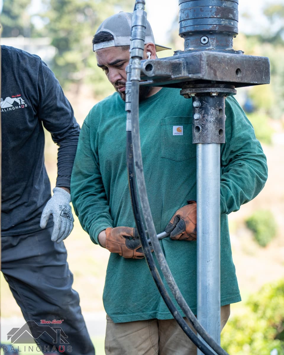 Crew member in a green shirt tightening a coupling bolt on a helical pier below the drive head