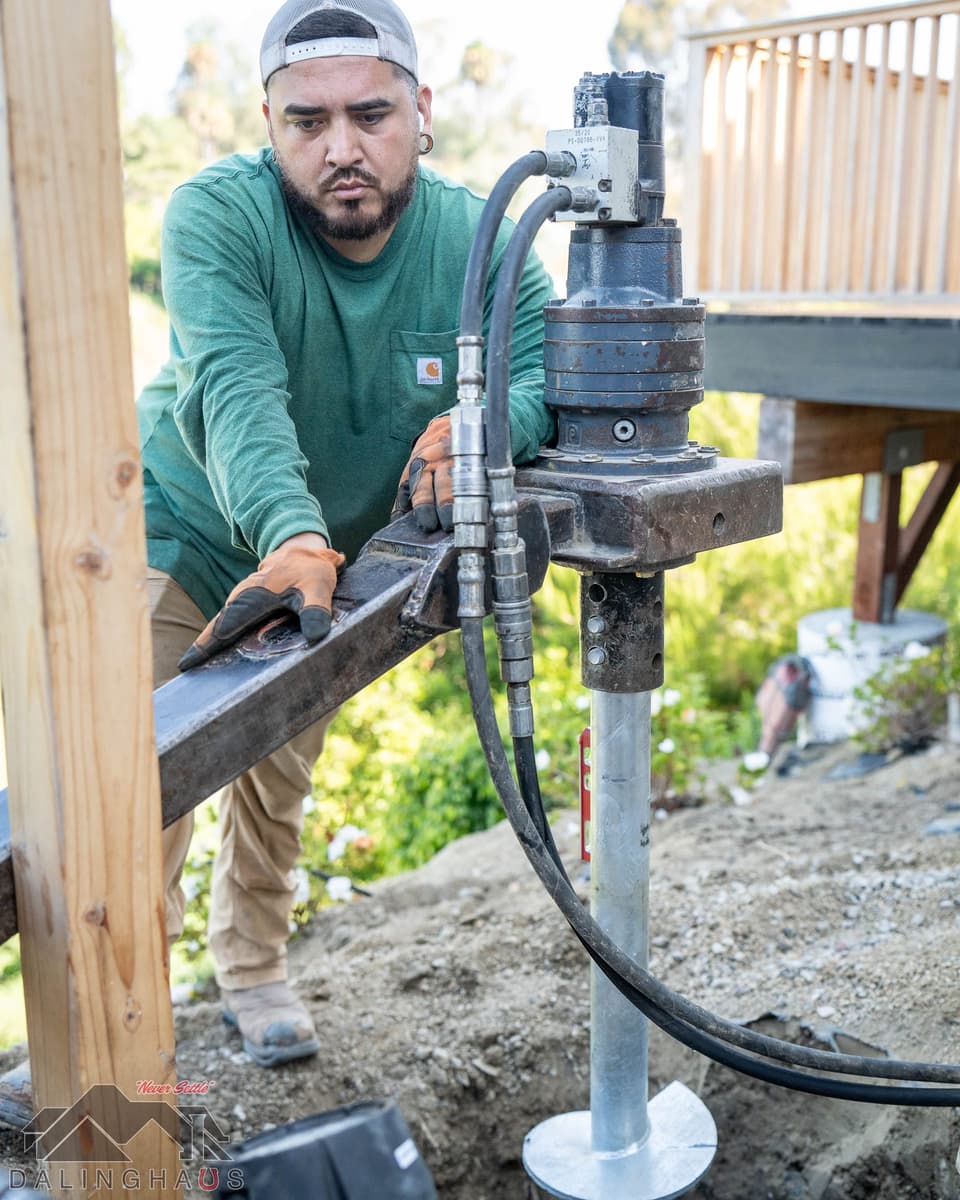 Crew member with both hands on the torque arm of a drive head on a helical pier, deck framing behind