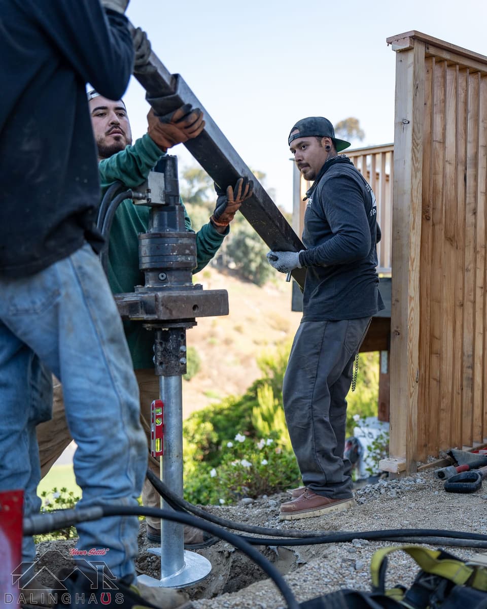 Crew positioning a torque arm on a hydraulic drive head beside a new wood deck screen, hillside behind