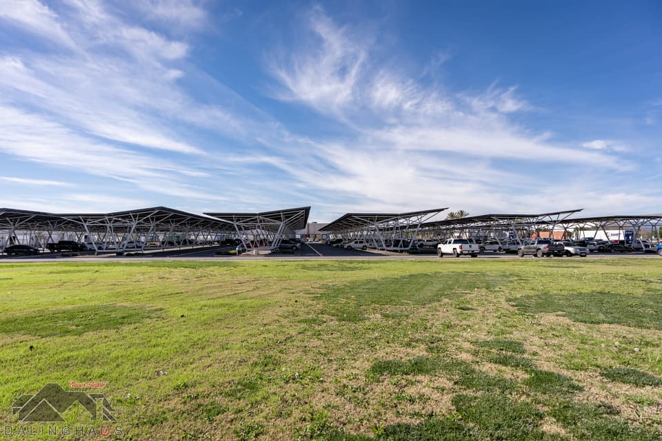The completed canopy field seen from a lawn, several parallel runs of solar panels on white steel columns under a wide sky with high cirrus cloud.
