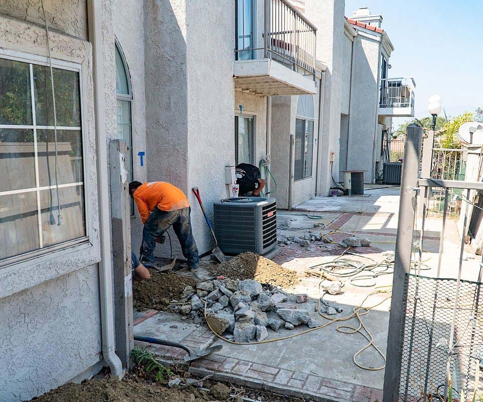 Crew working at the base of a stucco townhouse row, broken walkway concrete piled beside them