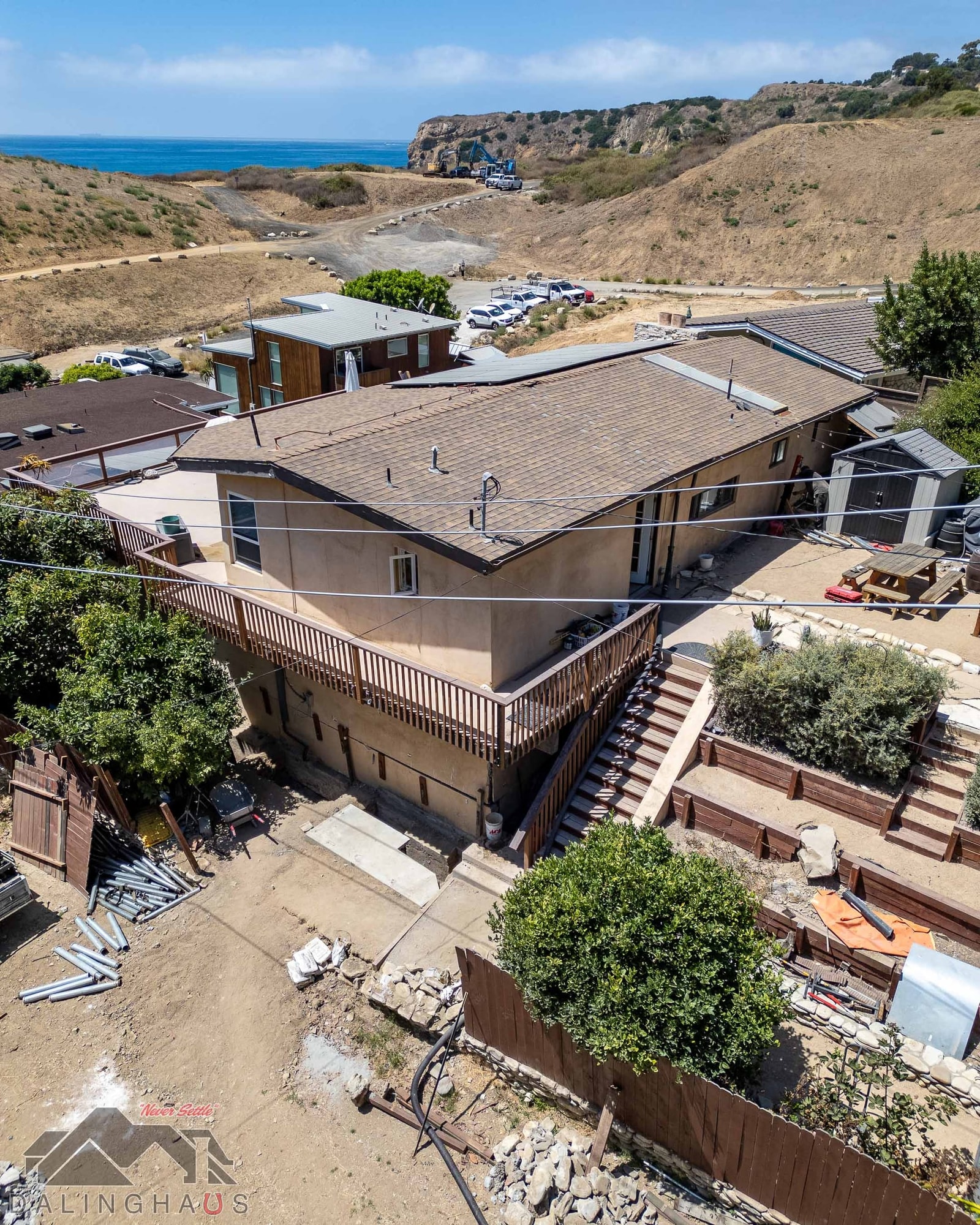 High angle of the two story stucco home, wood deck and stairs, steel pier sections stacked at the fence line
