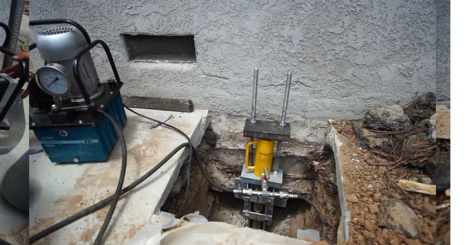 A Dalinghaus crew using a hydraulic ram to install steel push piers under a home's footing