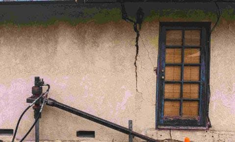 Push pier equipment set up beside a stucco wall with a vertical crack running down from the roofline