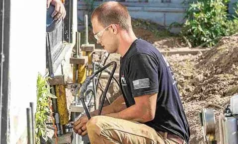 Technician running hydraulic lifting equipment on piers along a home's foundation while leveling a house
