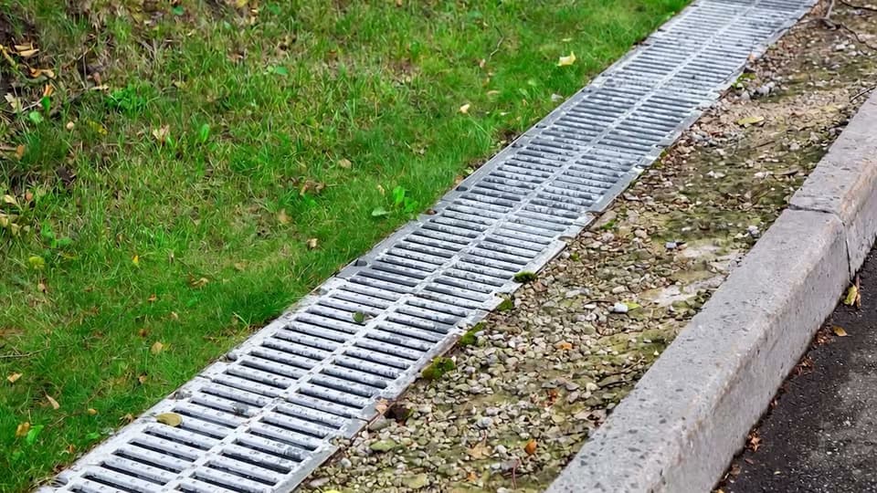 A surface drain with a metal grate, installed to carry storm water away from the foundation