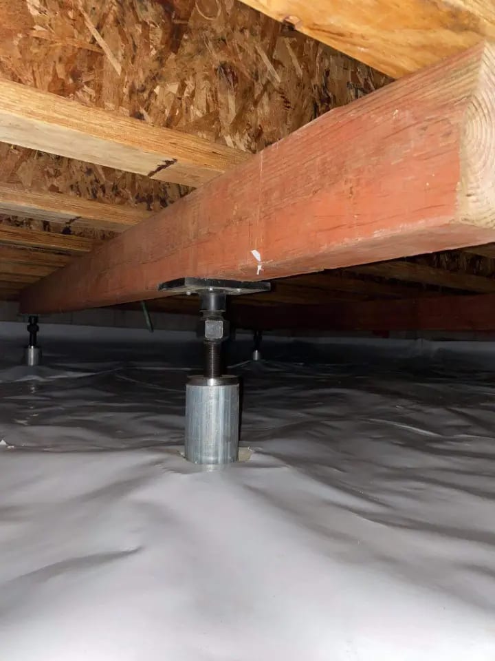 Adjustable steel jack post installed under a wooden girder in a crawl space