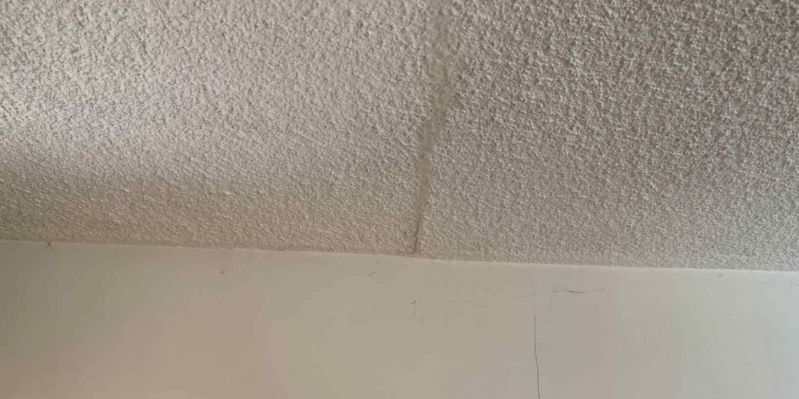 Crack running down a textured ceiling toward the joint where it meets the wall