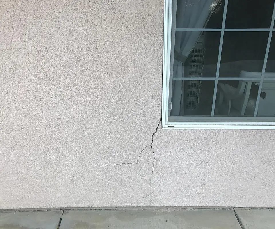 Stucco crack running down the wall from the corner of a window