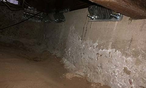 Concrete stem wall in a crawl space with white mineral deposits and flaking along its face