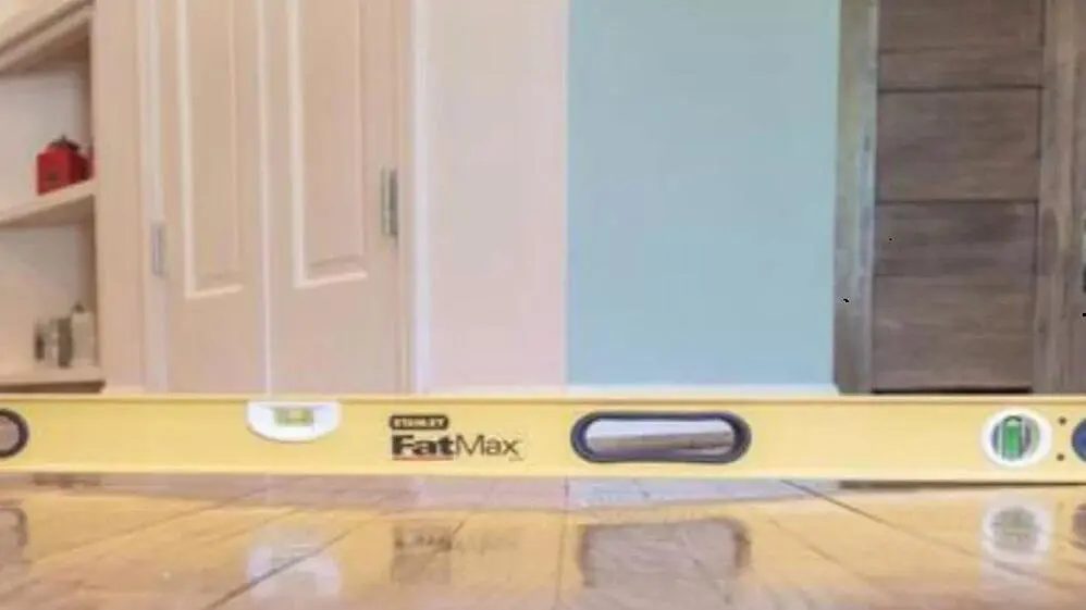 Spirit level resting on a wood floor in front of a closet door, checking the floor for slope